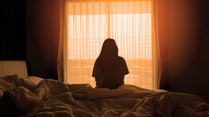 silhouette of woman sitting on the bed beside the windows with sunlight in the morning - Powered by Adobe