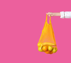 Woman holding net bag with fruits on pink background, closeup