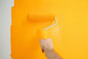 Obraz premium Man painting white wall with yellow dye, closeup. Interior renovation