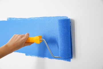 Woman painting white wall with blue dye, closeup. Interior renovation