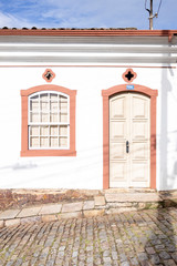 Front door and window pane of typical colourful facade with orange and brown warm tones on steep cobble street brightly lit by morning sun 