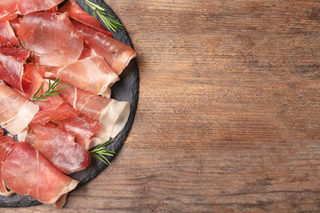 Pile of tasty prosciutto on wooden table, top view. Space for text