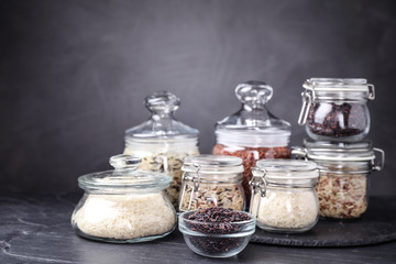 Brown and polished rice in jars on grey table