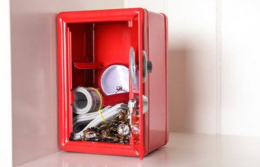 Open red steel safe with money and jewelry on shelf. Space for text