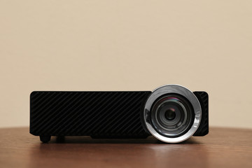 Modern video projector on wooden table against beige background