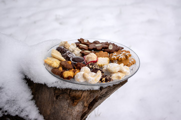 Many kinds of Christmas cookies on two cut glass transparent plates in white snow on wooden stump