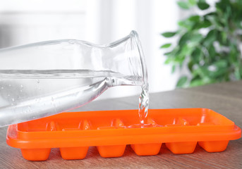 Woman pouring water into ice cube tray at wooden table, closeup