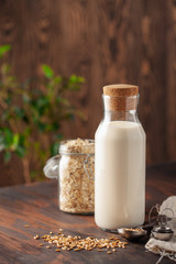 Vegan oat milk, non dairy alternative milk in a glass. Oat flakes  on wooden table.