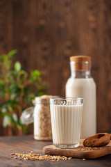 Vegan oat milk, non dairy alternative milk in a glass. Oat flakes  on wooden table.