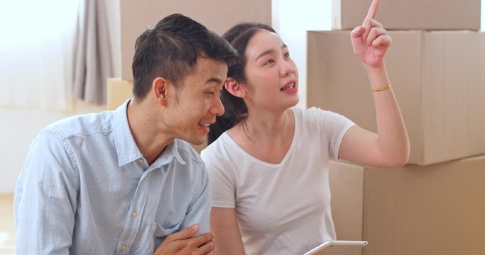 Young Happy Couple Moving In New Home, Sitting On The Floor And Shopping Online With Tablet