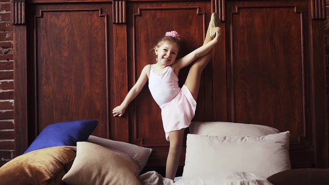 Athletic Baby girl in the splits in bed and laughs. Children's sports. Stretching and flexibility Slow motion