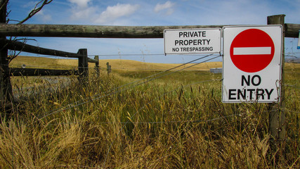 Landscape view of a farm land with wooden fence and warning signs. Lack of rain makes the grass...