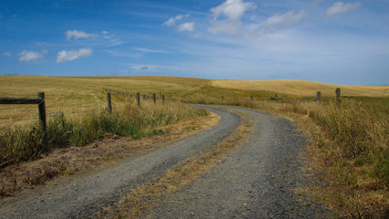 Windy driveway to enter a farmland with picturesque hills in the backgrorund. Summer in Australia is marked by lack of rain and constant heat