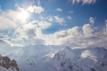 Naklejka premium The sun illuminates snow mountain peaks. White clouds.