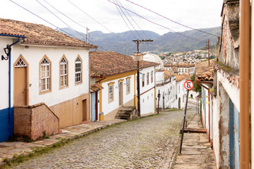 Steep descending cobble street of mining and colonial city in Minas with typical facades on either side leading past the mine museum of the Federal University
