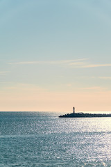 Clear sky and bright sunset over the sea with a breakwater and a lighthouse