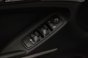Obraz na płótnie Canvas The control buttons for opening and closing windows of doors and electric controls and settings of mirrors on the door in black with leather upholstery in a luxury modern car.