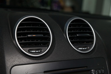 Fototapeta premium A close-up view of a part of the interior of a modern luxury car with a view of the ventilation chrome round deflector of the stove for heating and cooling the passenger compartment with black trim
