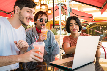 Three young friends using laptop at coffee shop.