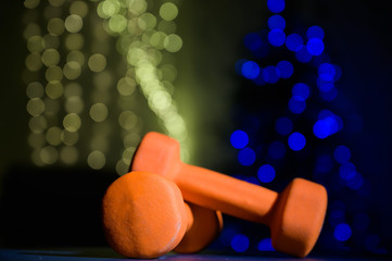 Two sports dumbbells on a black table against the background of Christmas lights on a Christmas tree.