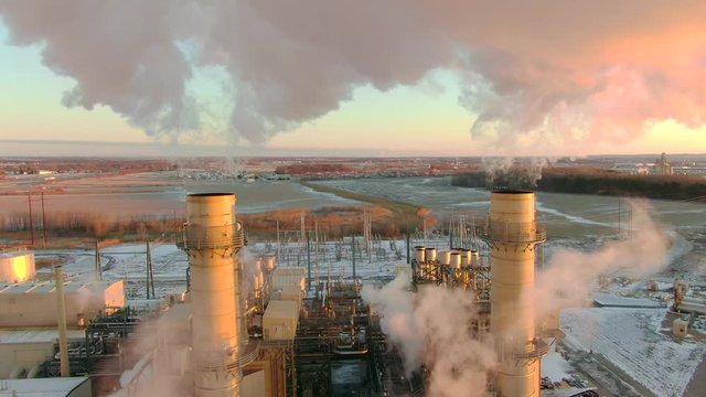 Moving aerial view of Factory or power plant emissions at sunrise, beautiful and colorful yet bad for the environment. The warm pink and yellow colors are due light from red sunrise.