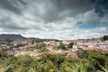 Fototapeta premium Panorama of colonial mining city centre Ouro Preto in Minas Gerais, Brazil, with surrounding mountains in the background seen from a high vantage point against a blue sky with dramatic clouds above