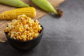 Popcorn in the black bowl and raw corn on the black table