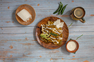 Fototapeta na wymiar presentation of mexican food with chilaquiles in green sauce, mexican coffee in folkloric cup with cheese, cream and chili peppers on blue wooden table