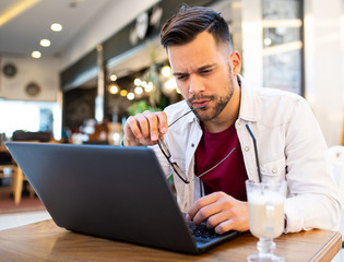 A young man focused over his laptop indoors.