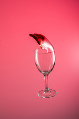 wine glass falls with a big splash of red wine flow on a red background