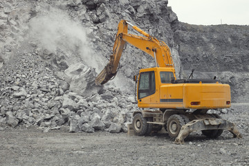 Excavator equipped with a hydraulic hammer works in a quarry, close-up.