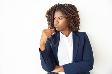 Businesswoman holding eyeglasses and looking aside. Young thoughtful African American businesswoman biting spectacles and looking away on white background. Business concept