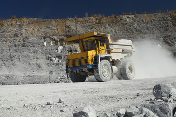 Large-capacity quarry dump truck in a dust cloud on the road in a quarry for limestone mining,...