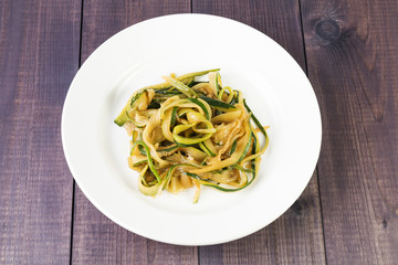 Zucchini spaghetti in a plate on a wooden background. Vegan food. Vegetable pasta