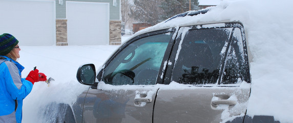 Female clearing winter snow from her car outside.
