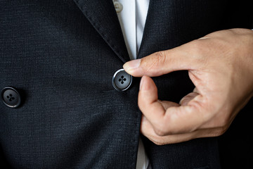 Close up of the man are wearing a black suit. The hands of men who are buttoned up on a black suit.