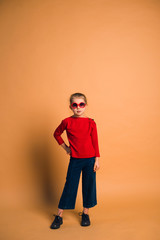 Fototapeta na wymiar Studio shot of young fashion 6-7 year old blonde girl wearing sunglasses, on light brown background