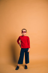Fototapeta na wymiar Studio shot of young fashion 6-7 year old blonde girl wearing sunglasses, on light brown background