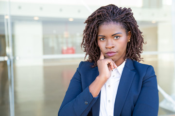 Fototapeta na wymiar Serious young businesswoman with hand on chin. Close-up portrait of attractive professional young African American businesswoman looking at camera. Professional concept