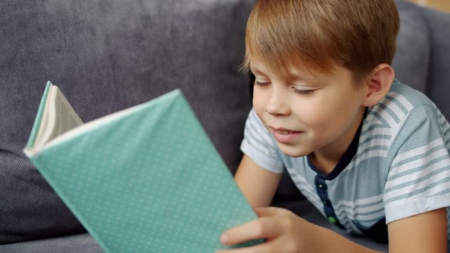 Slow motion of smiling small child reading book alone enjoying fairy-tale feeling happy and relaxed. Smart children, intellect and leisure time concept.
