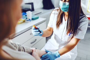 Female lab assistant in uniform, with protective mask and rubber gloves holding test tube with...