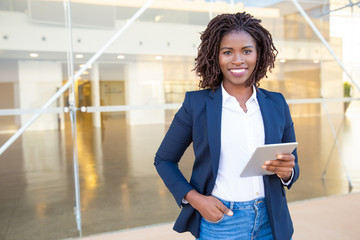Businesswoman holding tablet pc and smiling at camera. Cheerful young African American businesswoman holding digital tablet and looking at camera. Wireless technology concept - Powered by Adobe