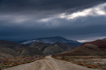 Dirt road to the mountains at stormy weather