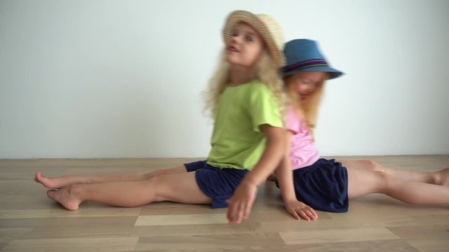 Funny little girls playing sitting on floor and waving looking at camera