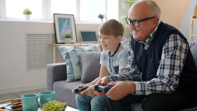 Joyful people old man and child are playing video game talking having fun in apartment together. Childhood, family and contemporary technology concept.