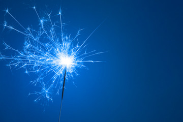 Christmas or Happy New Year party concept. Close up of Bright burning sparkler on a blue background.