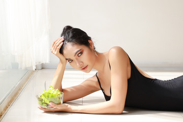 Obraz na płótnie Canvas close up beautiful healthy and sporty asian young woman holding salad bowl and eat after training ballet dancing while lying down