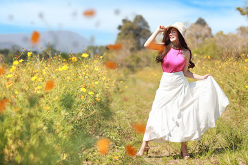 Asian beautiful woman, long hair in pink dress on yellow cosmos filed in winter with blue sky and mountain. Beautiful cute girl portrait with flowers in background. Travel in nature outdoor concept