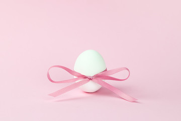 close-up Easter egg decorated with a pink bow on a pink background, festive minimalism. Holiday concept. Keto diet, a healthy food product.