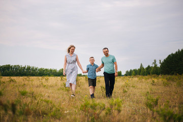 Naklejka na ściany i meble The boy leads the hands of his parents. Happy family in the fresh air. A family of three walking around the field